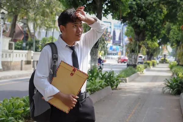 Beyaz gömlekli Asyalı bir iş arayanın portresi. İçinde özgeçmişi olan kahverengi bir zarfı tutarken iş arıyor. Şehir caddesinde aceleyle yürüyor. Personel alımı konsepti