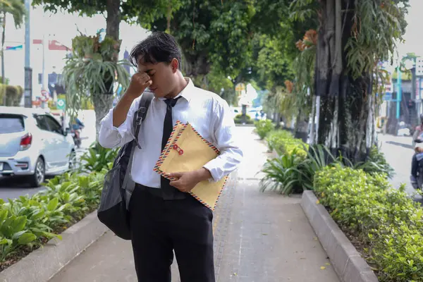 Takım elbiseli bir Asyalı iş arayanın portresi. Burnunu tutarken özgeçmişini içeren kahverengi bir zarf taşıyan bir iş arıyor. Personel alımı konsepti.