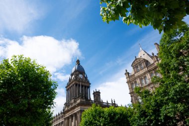 Leeds Belediye Binası, açık mavi gökyüzü altında büyüleyici bir mimari sergiliyor. Bölgeyi yemyeşil alan kaplıyor.