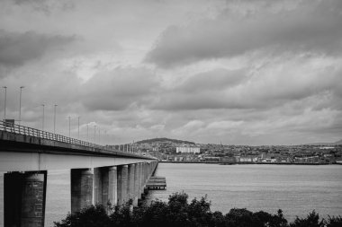Dundee İskoçya: 4 Ağustos 2024: Tay Köprüsü sakin bir su kütlesinin üzerine uzanır ve şehir manzarası üzerinde bulutlu bir gökyüzü bulunur