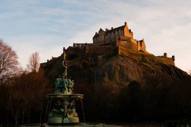 Edinburgh İskoçya: 13 Şubat 2024: Kışın Edinburgh Şatosu altın saat ışığında muhteşem görünüyor. Princes Street Gardens Ross çeşmesinden manzara