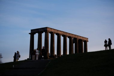 Edinburgh İskoçya: 13 Şubat 2024: Günbatımında Carlton Hill gözetleme noktasının tadını çıkaran turistler. Edinburgh şehrinin ufuk çizgisi