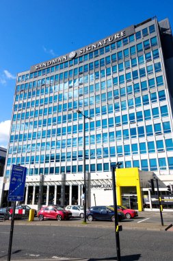 Newcastle UK: 8 Haziran 2024: Güneşli mavi gökyüzü gününde Sandman İmza Newcastle Oteli. Newcastle, İngiltere 'de gökyüzü ve bulutları yansıtan sayısız pencereli uzun bir otel.
