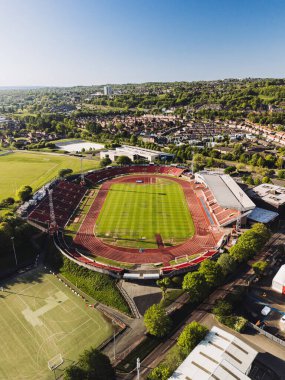 Gateshead UK: 10 Mayıs 2025: Gateshead Stadyumu, açık mavi bir gökyüzü altında yemyeşil tepeler ve şehir evlerinin zeminine kurulmuş, koltuk ve raylarla çevrili canlı yeşil bir sahaya sahiptir.