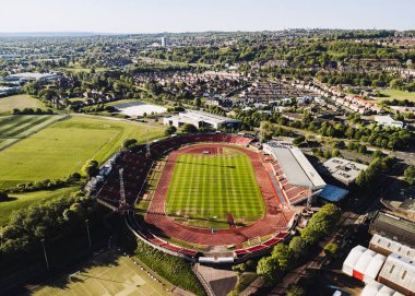 Gateshead UK: 10 Mayıs 2025: Gateshead Stadyumu, açık mavi bir gökyüzü altında yemyeşil tepeler ve şehir evlerinin zeminine kurulmuş, koltuk ve raylarla çevrili canlı yeşil bir sahaya sahiptir.