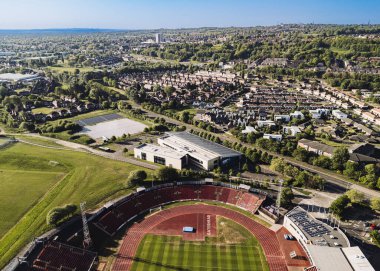 Gateshead UK: 10 Mayıs 2025: Gateshead Stadyumu, açık mavi bir gökyüzü altında yemyeşil tepeler ve şehir evlerinin zeminine kurulmuş, koltuk ve raylarla çevrili canlı yeşil bir sahaya sahiptir.