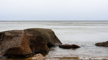 In the seascape, in the foreground, huge glacial pink granite stones - boulders. The horizon of the Baltic Sea is hidden in a cloudy haze resembling fog. Low, cloudy sky. Drizzle. Northern beauty