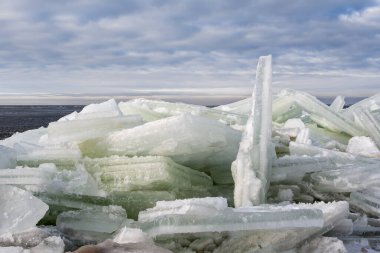 Baltık Denizi 'nde kıyı buzu uğulduyor. Kış günü bulutlu bir gökyüzünün arka planına karşı. Yumuşak güneş ışığı.