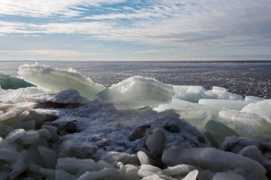 Deniz kıyısındaki buz kırıkları şeklinde mırıldanır. Karanlık donmuş deniz. Kısa bir kış gününün sonunda katmanlı bulutlar ve arka ve yan doğal sarı doğrudan güneş ışığı ile güzel alçak gökyüzü.
