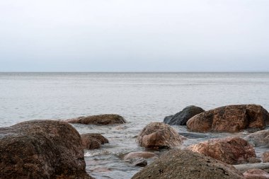 Sahil sularında, ön planda pembe granit kayalar olan deniz burnu. Bulutlu, ufka uzanan, gökyüzü. Deniz sakin - hafif bir esinti