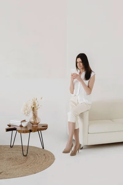 ソファの端に座っている間 スマートフォンを使用して白い魅力的な女性 コミュニケーションの概念 — ストック写真
