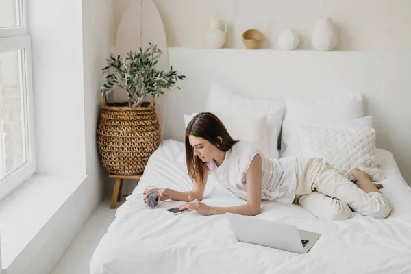 Χαλαρή Γυναίκα Ξαπλωμένη Στο Κρεβάτι Και Χρησιμοποιώντας Smartphone Και Laptop Royalty Free Εικόνες Αρχείου