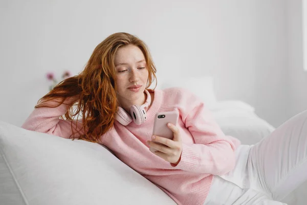 Красивая Молодая Рыжая Женщина Отдыхает Дома Диване Пользуется Мобильным Телефоном Стоковое Изображение