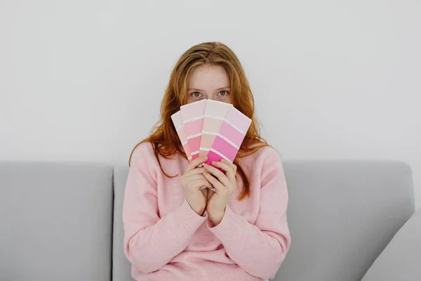 Redhead Woman Sitting Sofa Hiding Pink Paint Swatches Stock Image