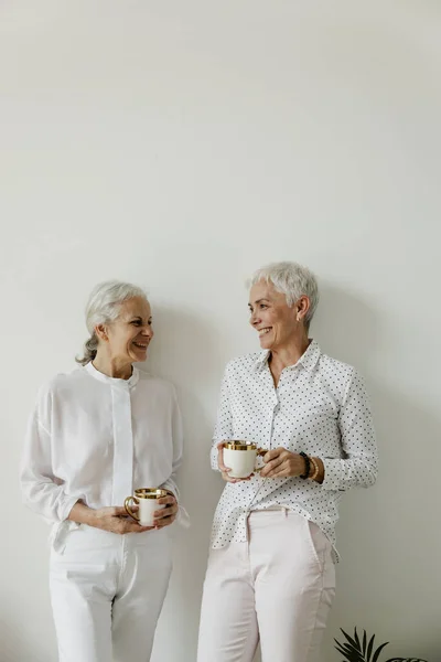Seniorinnen Trinken Kaffee Und Lachen Auf Weißem Wandhintergrund Mit Kopierraum Stockfoto