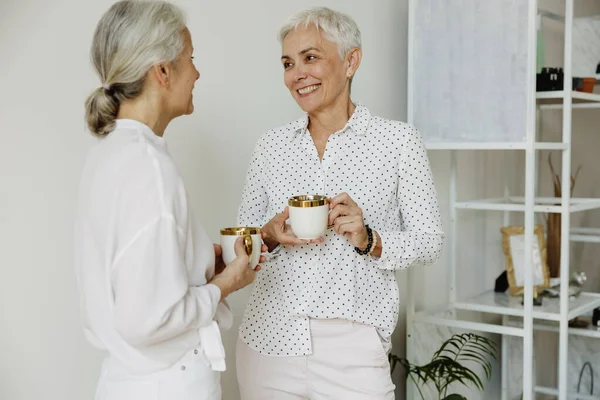 Two Smiling Stylish Middle Aged Female Drinking Coffee Chatting Modern Stock Photo