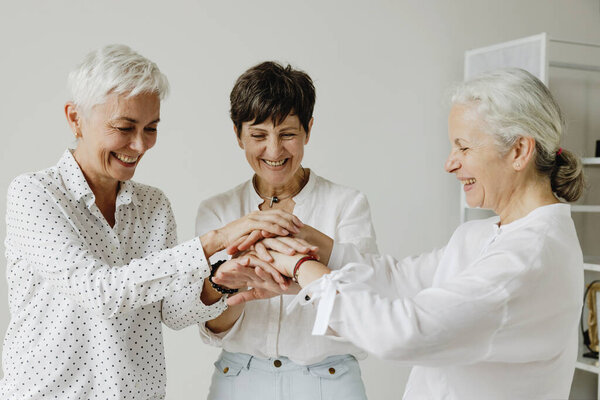 Three Confident Stylish Mature Women Stacking Hands Smiling Royalty Free Stock Photos
