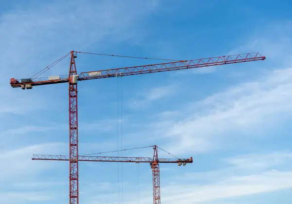 Construction cranes work on creation site on blue cloudy sky background
