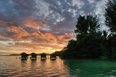 Waigeo Adası, Raja Ampat, Batı Papua, Endonezya sahillerindeki tipik su bungalovlarının üzerinde güzel bir günbatımı.