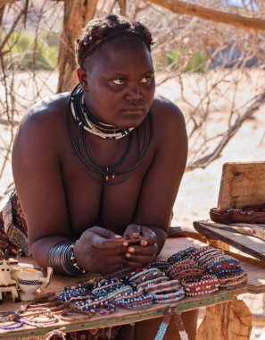 Kunene Bölgesi, Namibya, Afrika - 20.11.2023: Himba kabilesine özgü yerli kadın geleneksel el yapımı ürünler satıyor