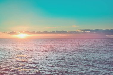 Pembe deniz sahilinden yumuşak dalgalarla izlenen renkli günbatımı