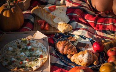 Doğada sonbahar pikniği, kruvasan, pizza, çikolata, meyve kompozisyonu, yiyecek ve içecek kavramı