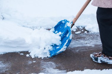 Kış sorunları konsepti. Bahçede kürekle kar kazan bir kadın. Mavi kürekli ve kar temizleyen bir bayan. Kış rutin konsepti.