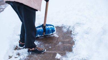 Kış sorunları konsepti. Bahçede kürekle kar kazan bir kadın. Mavi kürekli ve kar temizleyen bir bayan. Kış rutin konsepti.