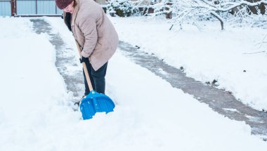 Kış sorunları konsepti. Bahçede kürekle kar kazan bir kadın. Mavi kürekli ve kar temizleyen bir bayan. Kış rutin konsepti.