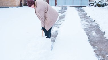 Kış sorunları konsepti. Bahçede kürekle kar kazan bir kadın. Mavi kürekli ve kar temizleyen bir bayan. Kış rutin konsepti.