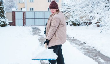 Kış sorunları konsepti. Bahçede kürekle kar kazan bir kadın. Mavi kürekli ve kar temizleyen bir bayan. Kış rutin konsepti.