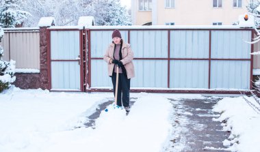 Kış sorunları konsepti. Bahçede kürekle kar kazan bir kadın. Mavi kürekli ve kar temizleyen bir bayan. Kış rutin konsepti.