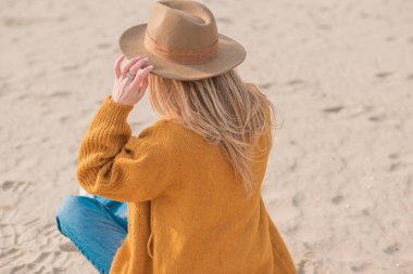 Yün sarısı hırkalı kadın, fötr şapka ve kumsalda kot pantolon, yeni koleksiyon, modaya uygun moda.
