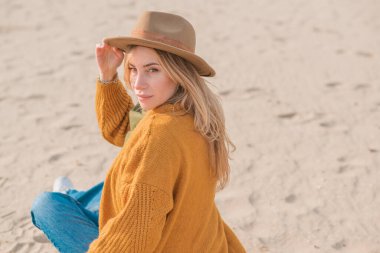 Woman in wool yellow cardigan, fedora hat and blue jeans at the beach, new collection, fashionable trend