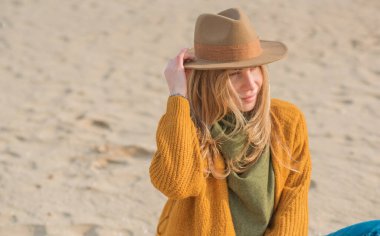 Woman in wool yellow cardigan, fedora hat and blue jeans at the beach, new collection, fashionable trend