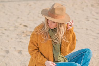 Woman in wool yellow cardigan, fedora hat and blue jeans at the beach, new collection, fashionable trend
