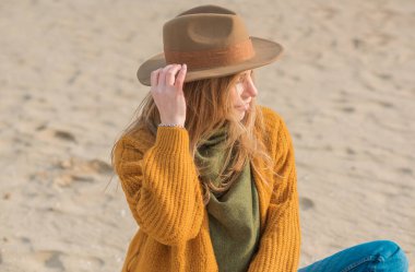 Woman in wool yellow cardigan, fedora hat and blue jeans at the beach, new collection, fashionable trend