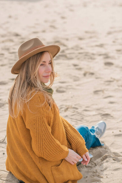 Woman in wool yellow cardigan, fedora hat and blue jeans at the beach, new collection, fashionable trend