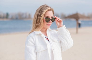  Beyaz ceketli kadın, güneş gözlüğü ve kumsalda kot pantolon, yeni koleksiyon, modaya uygun moda.