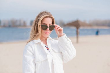 Beyaz ceketli kadın, güneş gözlüğü ve kumsalda kot pantolon, yeni koleksiyon, modaya uygun moda.