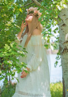 Doğadaki hassas gelin, beyaz dantelli ve çelenkli uzun sarı saçlı geleneksel Avrupalı bayan.   