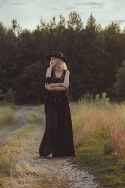 Çingene tarzı kadınlar için. Klasik Bohem tarzı, siyah pantolonlu kadın, fötr şapka ve ışıltılı bluz.