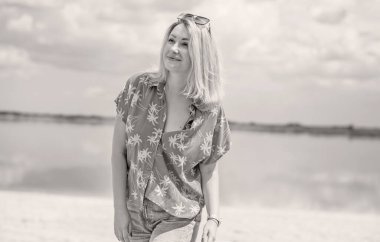 Tatil tarzı, kadın kıyafetleri. Genç Avrupalı bronz tenli, sarı saçlı, kot pantolonlu ve kumsalda renkli pamuklu gömlekli bir kadın.