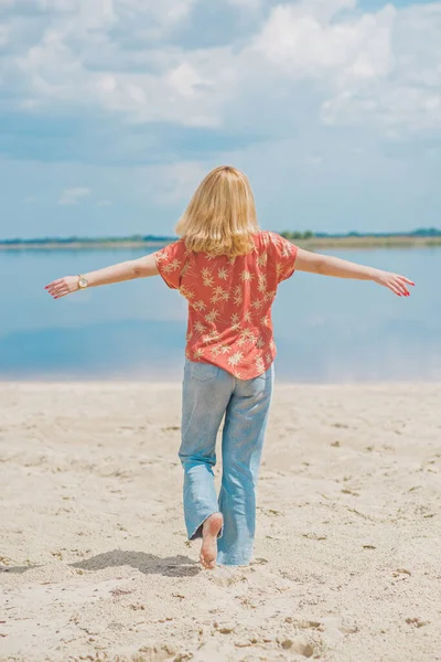 Vacation style, woman wardrobe. Illustration of young European tanned woman with blonde hair in blue jeans and colorful cotton shirt at the beach