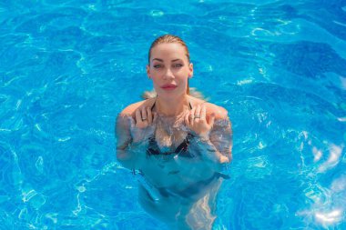 Havuzdaki Avrupalı sarışın güzel kadın. Seyahat ve tatil konsepti, mavi su ve bronz vücut