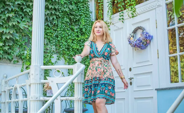 穿着花衣的漂亮的欧洲年轻女子站在阳台上 漂亮浪漫的房子庭院景观 — 图库照片