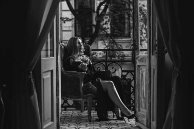 Peignoir giymiş bir kadın ve bir kadeh şarap. Tüylü siyah ipek bornozlu Avrupalı sarışın kadının şehvetli fotoğrafı. Moda konsepti