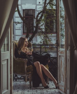 Peignoir giymiş bir kadın ve bir kadeh şarap. Tüylü siyah ipek bornozlu Avrupalı sarışın kadının şehvetli fotoğrafı. Moda konsepti
