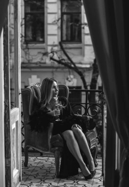 Peignoir giymiş bir kadın ve bir kadeh şarap. Tüylü siyah ipek bornozlu Avrupalı sarışın kadının şehvetli fotoğrafı. Moda konsepti