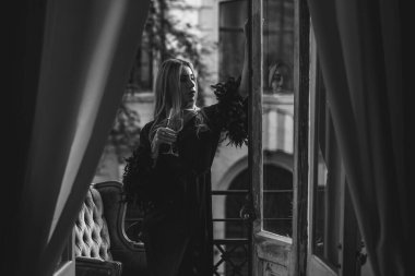 Peignoir giymiş bir kadın ve bir kadeh şarap. Tüylü siyah ipek bornozlu Avrupalı sarışın kadının şehvetli fotoğrafı. Moda konsepti